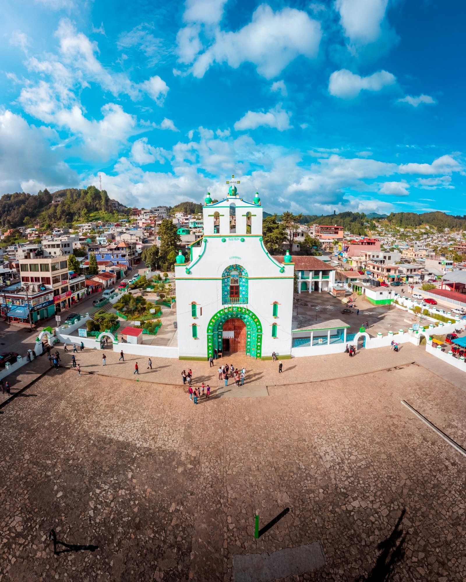 Iglesia color verde con blanco en medio de una plaza, con persona alrededor, en un pueblo lleno de casas de colores, y recuerdo para nuestras experiencias.