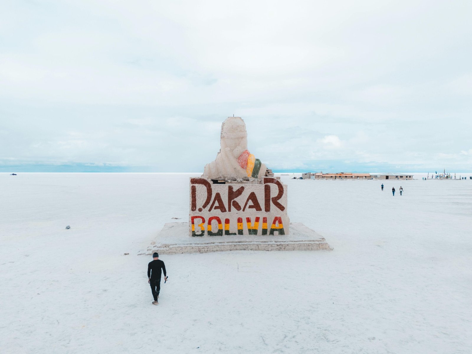 Monumento dedicado al Dakar, ubicado en el salar de Uyuni en Bolivia, con algunos turistas a los al rededores que pasan por la ruta que cruza el salar o se dirigen a la plaza cercana, formando parte de una de las Rutas para viajar por Sudamérica.