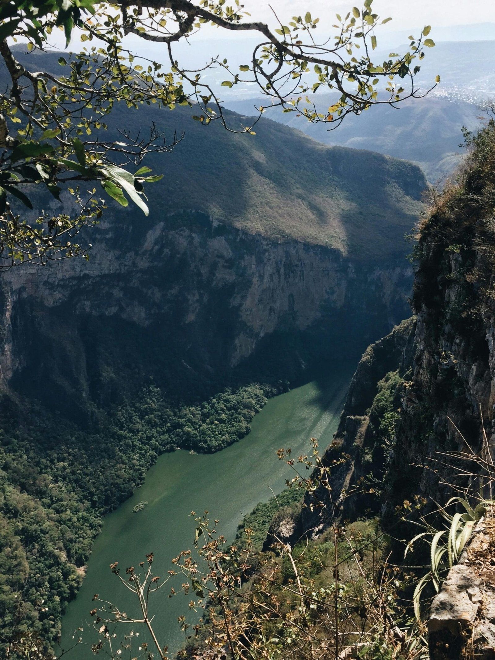 Un paisaje natural, un río tranquilo que se abre paso entre dos enormes paredes de roca, las montañas son altas, imponentes y están cubiertas parcialmente de vegetación, con un ambiente fresco, es un cañón profundo rodeado.