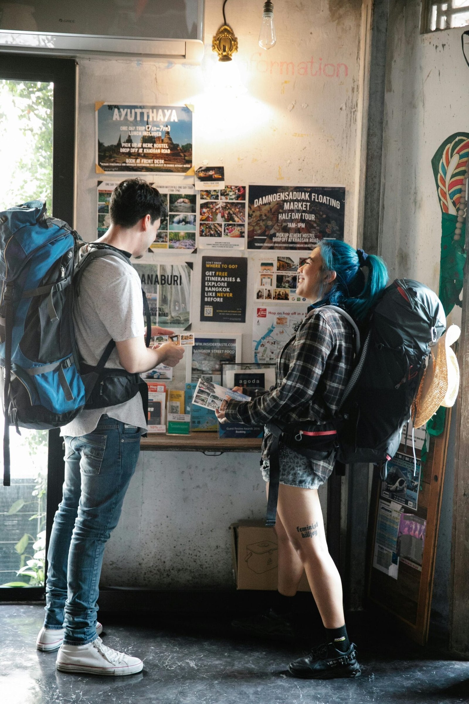 Turistas mochileros frente a un muro con diferentes carteles que los invitan a vivir nuevas experiencias, visitando diferentes destinos, siguiendo diferentes rutas y llendo a algunos restaurantes.