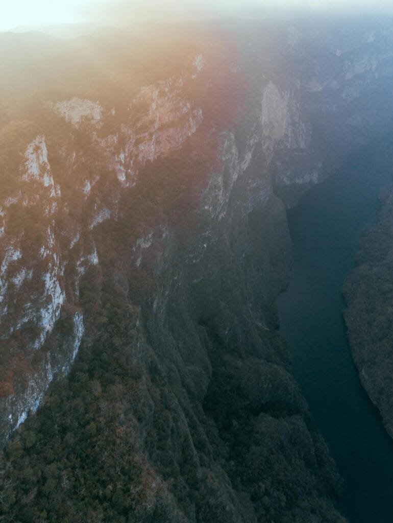 Un paisaje natural, un río tranquilo que se abre paso entre dos enormes paredes de roca, las montañas son altas, imponentes y están cubiertas parcialmente de vegetación, con un ambiente fresco, es un cañón profundo rodeado de naturaleza, un lugar que transmite grandeza.