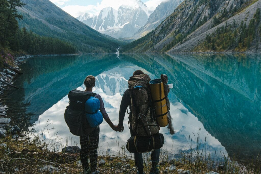 Una pareja de excursionistas se toma de la mano mientras contempla un impresionante lago de aguas cristalinas, rodeado de montañas nevadas