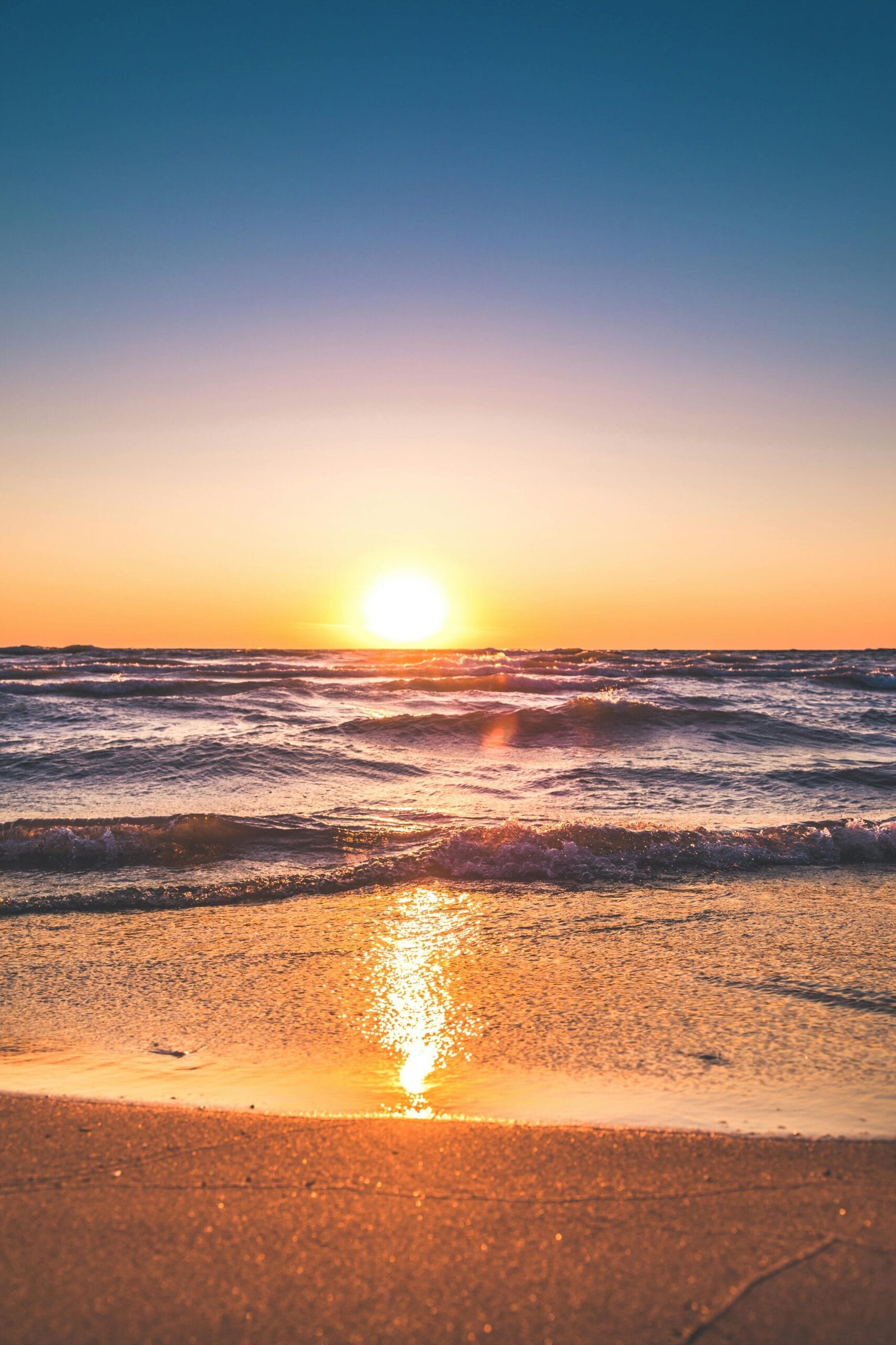 Playa en el atardecer, el mar es iluminado por la luz del sol y la arena clara color dorada es iluminada por los rayos del sol