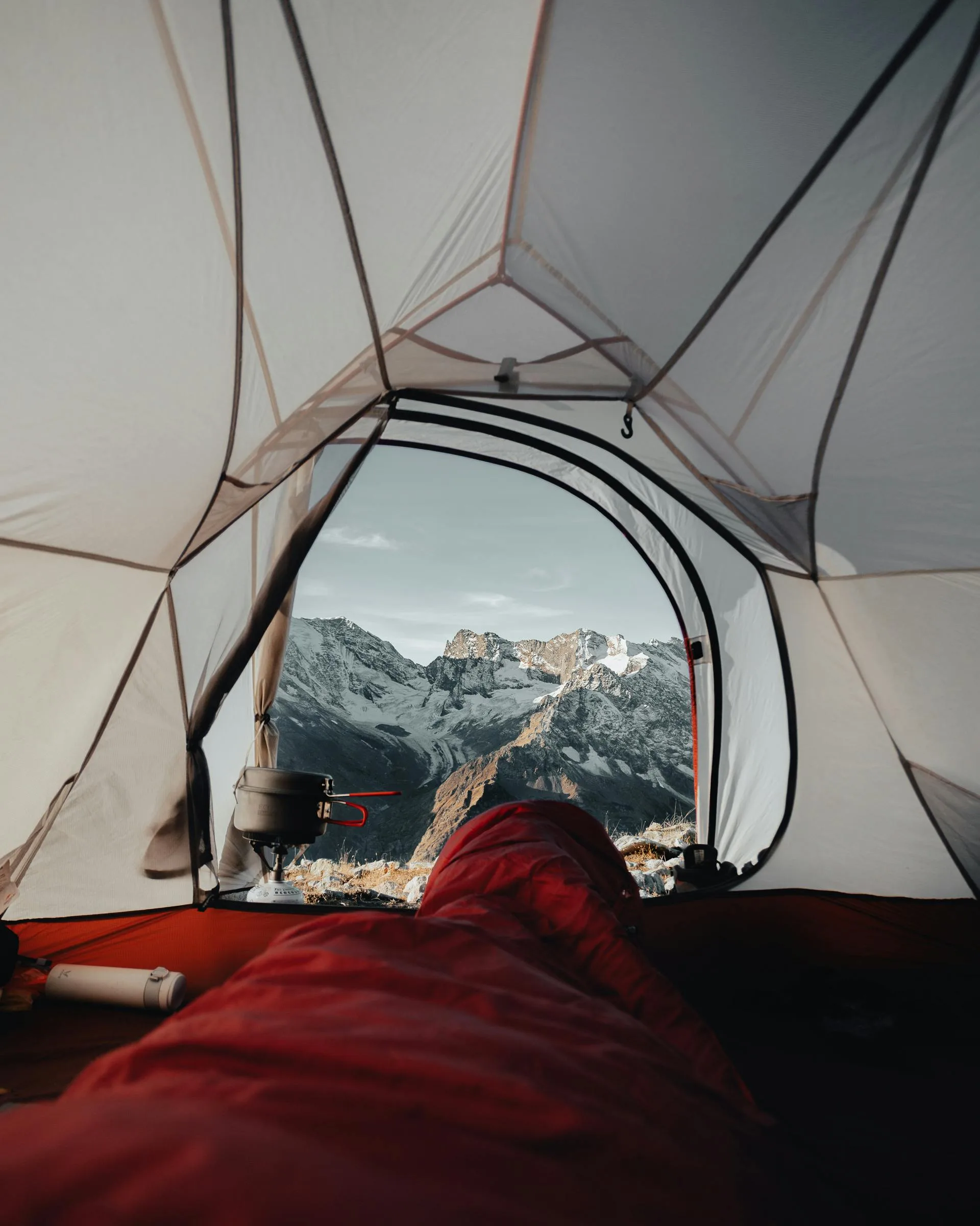 Saco para dormír que es parte de nuestros Productos para mochileros, dentro de una casa de campaña con equipo para acampar, en una montaña nevada con fondo de montañas nevadas.